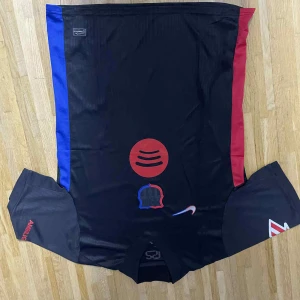Svart FC Barcelona fotbollströja Nike - Säljer en svart FC Barcelona fotbollströja från Nike med röda och blå sidopaneler. Tröjan har korta ärmar, tryck med Spotify-logga och klubbmärke på framsidan samt UNHCR-tryck på ryggen. Materialet är lätt och andas, perfekt för match eller träning.