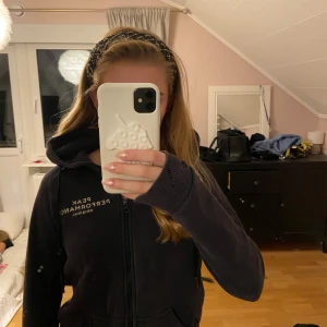 Svart hoodie Peak Performance XS - Svart hoodie från Peak Performance i storlek XS. Tröjan har huva med snörning, dragkedja framtill och vit logotyp på bröstet. Mjukt fleecefoder på insidan och ribbade muddar vid ärmslut. Säljer billigt för hålet på ärmen, men det syns egentligen inte så mycket❣️