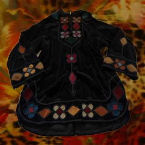 Retro tröja  - Unik svart klänning/tröja i sammet med färgglada broderade mönster i rött, blått, beige och grönt. Den har långärmade utsvängda ärmar och geometriska former längs halsringning, ärmar och nederkant. Perfekt för dig som gillar bohemisk och retro stil.