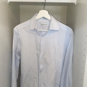 Randig skjorta från These Glory Days - Snygg slim fit skjorta från These Glory Days i italienskt tyg. Skjortan är vit med tunna ljusblå ränder. Storlek m. Mycket bra skick. Hör av dig vid fler frågor