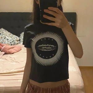 T-shirt - Den passar alla tre storlekar jag skrivit ner beroende på hur man vill att den ska sitta. Svart croppad t-shirt från New Yorker med ett stort vitt grafiskt tryck framtill som ser ut som en sol eller stjärna. Rund halsringning och korta ärmar. Perfekt för dig som gillar streetstyle och vill ha en edgy vibe.