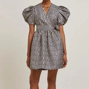 Mönstrad klänning By Malina - Supersnygg kortklänning från By Malina med svart och beige mönster, puffiga korta ärmar och omlott-v-ringning. Materialet är glansigt och känns lyxigt, perfekt för att sticka ut. Liten i storlek skulle säga passa mer M.