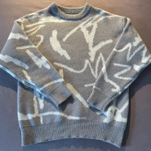 Grå stickad tröja med abstrakt mönster - Säljer en grå stickad tröja med vitt abstrakt mönster. Tröjan har rund halsringning, ribbade muddar och nederkant. Riktigt varm och mysig tröja som passar perfekt nu till sen hösten och vintern. Tröjan är helt oanvänd. Den är storlek M men passar M/L. Det är bara att höra av dig om du har någon fundering :)
