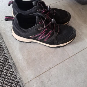 Svarta sneakers med rosa detaljer - Svarta sneakers med rosa detaljer och snörning med snabbspänne. Ovandel i slitstark textil och syntet, sula i beige och svart. Perfekta för dig som gillar en sportig och bekväm stil. Vattenavvisande material från Gore-Tex. 25,6cm inuti 