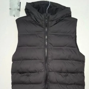 Superfin svart dunväst med huva stl 140 från Zara - Snygg svart dunväst med huva och dragkedja framtill. Västen har ett quiltat mönster och två fickor med knappstängning. Perfekt för lager-på-lager och chill stil. Passar dig som gillar enkel och clean look.