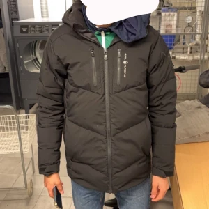 Svart pufferjacka från sail racing - Svart pufferjacka från sail racing med huva och två bröstfickor med dragkedja. Jackan har en quiltad design och hel dragkedja framtill. Perfekt för kalla dagar och har en clean, sportig look.