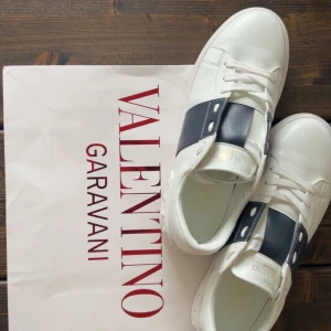 Valentino Garavani Open sneakers vit/svart - Kan diskutera pris mycket. Snygga Valentino Garavani Open sneakers i vitt skinn med bred svart läderdetalj över vristen och ikoniska nitar på hälen. Klassisk rund tå, platt sula och snörning framtill. Perfekta för dig som vill ha en lyxig och stilren look.