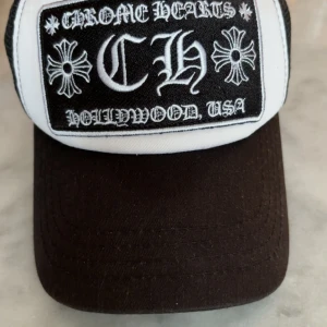 Chrome Hearts truckerkeps svart/vit - Snygg truckerkeps från Chrome Hearts i svart och vitt med broderad logga och text 'Hollywood USA' framtill. Kepsen har mesh på baksidan och metallknapp med logga. Perfekt för dig som vill sticka ut med streetstyle och exklusiv känsla. Hör av vid frågor eller funderingar!!