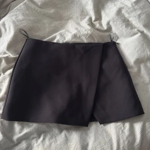 Svart omlottkjol från Zara - Stilren svart kortkjol från Zara i omlottmodell med shorts under. 