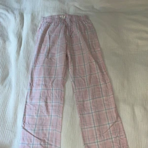 Rosa rutiga byxor från Gina Tricot - Mysiga byxor från Gina Tricot i ljusrosa med rutigt mönster i vitt och ljusblått. De har resår i midjan och snörning för extra komfort. Perfekta för chill dagar hemma eller som pyjamasbyxor.