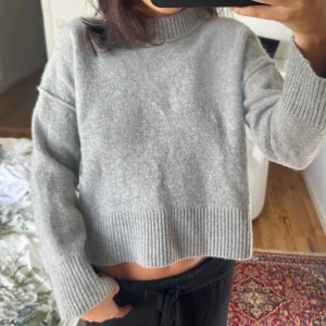 Grå stickad tröja - Mysig grå stickad med hög hals och breda ribbade muddar vid ärmslut och nederkant. 