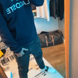 Mörkblå hoodie från Lacoste - Säljer en mörkblå hoodie från Lacoste med stor logga och krokodil på bröstet. Tröjan har huva, magficka och långa ärmar. Perfekt för dig som gillar streetwear och vill ha en klassisk look med snygg passform. Storlek S, passar folk runt 180! Ifall du har funderingar eller frågor så skicka iväg ett dm!
