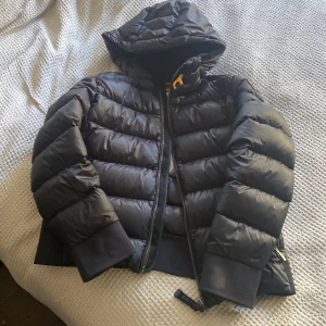 Svart dunjacka Parajumpers Sheen - Säljer en svart dunjacka från Parajumpers, modell Sheen. Jackan har en puffig design med huva, breda muddar och dragkedja framtill. Perfekt för kalla dagar och har en riktigt snygg streetstil. Klassisk logga på ärmen och coola detaljer. Helt oanvänd