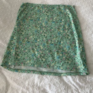 Mintgrön blommig kortkjol och topp sett  - Superfin mintgrön kortkjol och topp med blommigt mönster i vitt, blått, gult och rosa. Kjolen har en rak passform och är sydd i ett mjukt, stretchigt material som känns bekvämt. 