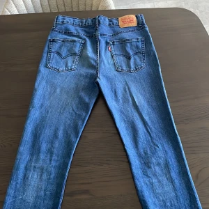 Levi's 512 Slim Taper jeans blå - Säljer ett par Levi's 512 Slim Taper jeans i klassisk blå tvätt. Jeansen har fem fickor, smal passform och avsmalnande ben. Ikonisk läderpatch bak i midjan och Levi's röda etikett på bakfickan. Perfekta för en stilren och modern look.