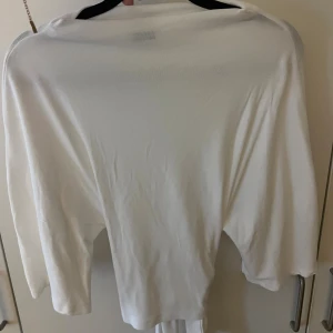 Vit omlottopp från Gina Tricot - Säljer en vit omlottopp från Gina Tricot i mjukt material. Toppen har trekvartsärm och knytband i midjan för en snygg passform. Perfekt att styla med jeans eller kjol för en fräsch look.