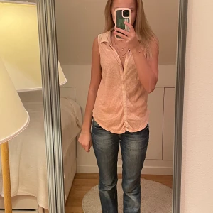 Ljusrosa Hollister blus  - Säljer en ljusrosa ärmlös blus med klassisk krage och knäppning framtill. Toppen har en avslappnad passform och är tillverkad i ett tunt, mjukt tyg som känns svalt. Perfekt för varmare dagar och enkel att styla med jeans eller kjol.