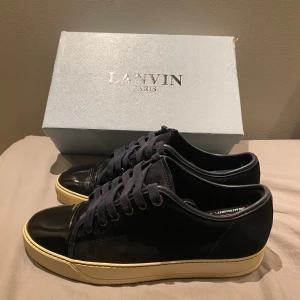 Lanvin marinblåa  sneakers i mocka och skinn - Snygga marinblåa  sneakers från Lanvin med ovandel i mocka och detaljer i blankt skinn på tån. Skorna har mörkblå snörning, metallöljetter och en kontrasterande beige sula. Perfekta för dig som gillar stilrena och exklusiva sneakers. Sulan är mycket finare i verkligheten. Storlek UK 7 vilket motsvarar 42/43