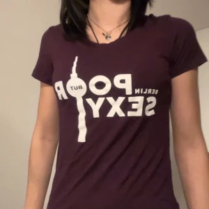 Mörklila Berlin t-shirt med tryck -  t-shirt från Fat Tire Bike Tours jag köpte ifrån Berlin med tryck ’Berlin Poor but Sexy' och baksidan har en cykel och Berlin-tryck med korta ärmar använt bara en gång 