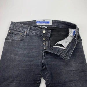 Jacob Cohën jeans  - Snygga svarta jeans från Jacob Cohën i klassisk femficksmodell. Jeansen har en mörk tvätt, silverfärgade knappar och diskreta slitningar. Tillverkade i mjukt denimtyg med en rak passform som passar till det mesta.