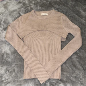 Beige ribbad tvådelad topp från 4th Reckless - Säljer en beige tvådelad topp från 4th Reckless i storlek 36. Setet består av en ribbad ärmlös linnetopp med v-ringning och en croppad långärmad bolerotopp i samma stickade material. Perfekt för att skapa en cool lager-på-lager look.