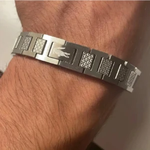  armband från Lacoste (helt ny+gratis frakt) - Stilrent armband i silverfärgad metall från Lacoste med klassisk krokodil-logga. Länkarna har ett snyggt rutmönster och armbandet har en robust känsla. Perfekt accessoar för dig som gillar en sportig och modern look.