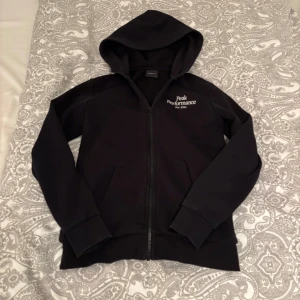 SVART JR ORIGINAL ZIP HOOD - Svart kofta från Peak Performance med dragkedja och broderad vit logga på bröstet. Tröjan har huva, långa ärmar och två fickor. Storlek 160, original pris 899! Pris kan diskuteras.