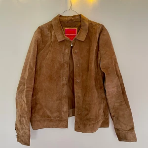 Brun mockajacka - Snygg brun vintage mockajacka med klassisk krage och knäppning framtill. Jackan har en stilren design och långa ärmar, perfekt för dig som gillar en clean och tidlös look. Storlek på jackan XL men snarare en M i passform. 