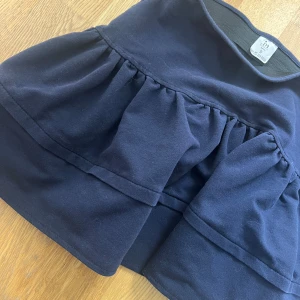 Mörkblå volangkjol från Impress - Supersöt mörkblå kortkjol i bomull. Fin att ha med en stor stickad tröja till