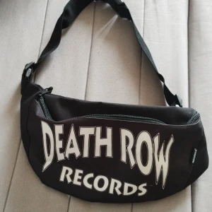 Death Row Records svart midjeväska  - Svart midjeväska med stort Death Row Records-tryck i vitt framtill. Väskan har justerbar rem och dragkedja upptill. Tillverkad i slitstark polyester och har en clean, rektangulär form som passar perfekt för att bära dina essentials.