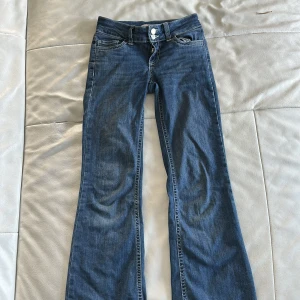 Blå bootcut jeans från Nelly - Snygga blå jeans från Nelly med bootcut passform och klassisk femficksdesign. Jeansen har dubbla knappar i midjan och coola detaljer på bakfickorna. Tillverkade i jeansmaterial och perfekta för dig som gillar en avslappnad men trendig look.