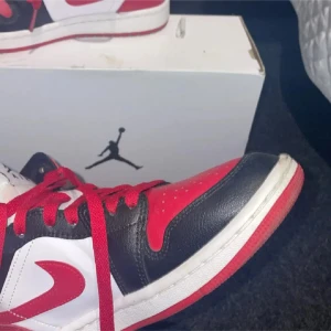 Nike Air Jordan 1 Chicago sneakers - Säljer ett par Nike Air Jordan 1 Chicago sneakers med klassisk färgblockning i rött, svart och vitt. Skorna har snörning, rund tå och platt sula. Ikonisk Jumpman-logga på tungan och Wings-märke på sidan. Tillverkade i skinn med röda skosnören och vit mellansula.