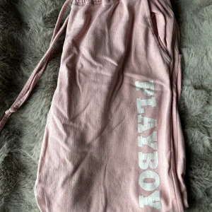 Rosa mjukisbyxor från Playboy - Säljer ett par ljusrosa mjukisbyxor från Playboy med vit logga längs benet. Byxorna har resår och snörning i midjan för skön passform. De är välanvända och därför lite noppriga