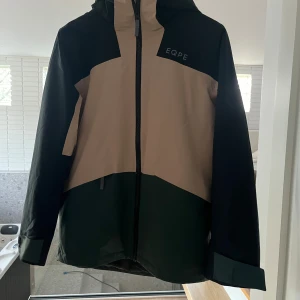 EQPE vindjacka i svart och beige - Snygg vinterjacka från EQPE.. Jackan har huva, hel dragkedja framtill och logga på bröstet.