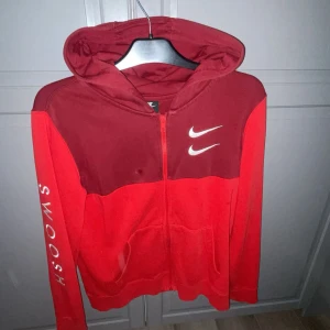 Röd Nike hoodie med dragkedja XL jr 158-170 - Nike hoodie i två nyanser av rött med hel dragkedja och huva. Swoosh-logga på bröstet och text på ena ärmen. Storlek XL jr (158-170cm) inte ren men säljs tvättad såklart. Perfekt för chill eller träning.