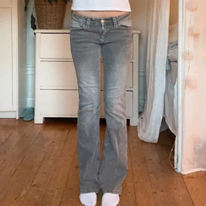 Grå bootcut jeans med detaljerade bakfickor - Snygga grå jeans med bootcut passform och låg midja. Jeansen har coola bakfickor med knapp och flätad kant, klassisk femficksdesign och dragkedja fram. Perfekta för dig som gillar en avslappnad men ändå trendig look.  Mått:📏   Innerbenslängd= 79cm Midjemått rakt över= 35cm