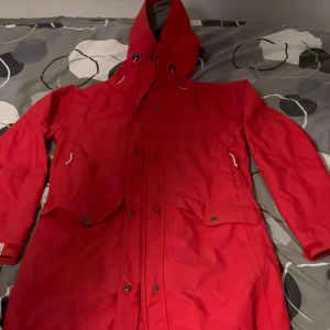 Röd parkas från Didriksons, strl 38 - Säljer en röd parkas från Didriksons i storlek 38. Jackan har huva med snörning, stora fickor med knappar och dragkedja framtill. Perfekt för kalla och blåsiga dagar, med klassisk Didriksons-brodyr på bröstet och Storm System-teknologi.