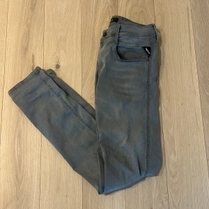 Replay grå slim jeans, Anbass - Säljer ett par gråa jeans från Replay med klassisk femficksdesign och svarta detaljer på fickorna. Jeansen har en slim passform och är tillverkade i mjukt denimtyg som sitter snyggt längs benen. Perfekta för dig som gillar stilrena och moderna jeans. Strl: W30 L32. Hör av er vid fler bilder!