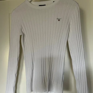 Vit ribbad tröja - Säljer en vit, ribbstickad tröja från GANT i storlek XS. Tröjan har lång ärm, rund halsringning och diskret GANT-logga på bröstet. 