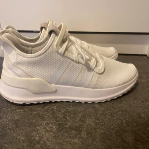 Vita Adidas sneakers med snörning - Fräscha vita Adidas sneakers med klassiska tre ränder på sidan. Ovandelen är i mesh och syntet, vilket ger en sportig vibe och skön ventilation. Platt sula och rund tå, med snörning och detaljer i ljusbeige på plösen. Perfekta för dig som gillar stilrena och cleana sneakers. ANVÄNDA 3-4 gånger max.
