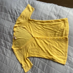 Gul kortärmad blus från Lykke - Superfin gul blus från Lykke med v-ringning och korta ärmar. Blusen har en rad med små knappar framtill och är gjord i ett mjukt, tunt material som känns skönt mot huden. Perfekt för dig som gillar färg och vill ha en enkel men snygg topp.använd 1 gång.