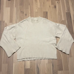 Beige stickad tröja från Gina Tricot - Beige stickad tröja från Gina Tricot i oversized modell. Tröjan har breda ribbade muddar vid ärmslut och nederkant samt en ribbad rund halsringning. Perfekt för lager-på-lager och chill vibes. Har även en slits på var sida.