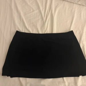 Svart enkel kortskort  - En stilren svart kortkjol med rak passform. Kjolen är helfärgad utan detaljer eller mönster och har en klassisk, minimalistisk look som är lätt att matcha med olika toppar och skor. Det är en skort alltså en kjol med shorts under. Aldriga använda 