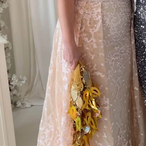 Champagnefärgad långklänning med spets - Säljer en elegant champagnefärgad långklänning med vackra spetsdetaljer och blommigt mönster. Klänningen har en figurnära överdel och ett svepande skirt tyg som ger en lyxig känsla. Perfekt för bal eller nyår. Materialet är troligtvis polyester eller siden.