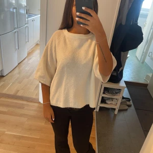 Vit stickad tröja med korta ärmar - Säljer en vit stickad tröja med avslappnad passform och korta, breda ärmar. Tröjan har rund halsringning och ribbade detaljer vid hals och nederkant. Perfekt för dig som gillar en enkel och clean look.