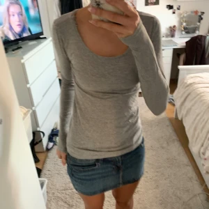 Grå långärmad topp med rund hals - Enkel och stilren grå långärmad topp med rundad halsringning. Modellen är figurnära och passar perfekt till jeans eller kjol. Mjuk och stretchig känsla, perfekt för lager-på-lager. Snygg basic som funkar året runt.