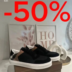 Burberry sneakers med klassiskt rutmönster - Snygga Burberry sneakers i svart med klassiskt rutmönster i beige, brunt och vitt på hälen. Skorna har vit platt sula, svarta snören och en stilren design. Perfekta för dig som vill ha en lyxig och trendig look med ikoniska detaljer.