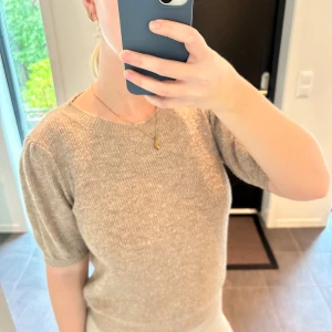 Beige stickad tröja med puffärm - Superfin beige stickad tröja med kort puffärm och rund halsringning. Tröjan har en ribbad struktur och är i ett mjukt material som känns skönt mot huden. Perfekt för dig som gillar en enkel men ändå trendig look.