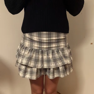 Rutig volangkjol från Bershka  - Supersöt kort kjol från Bershka i storlek XS. Kjolen är rutig i beige och svart med två volanglager som ger en riktigt trendig vibe. Perfekt för dig som gillar en lekfull och snygg stil. Resår i midjan för extra komfort. Aldrig använd 