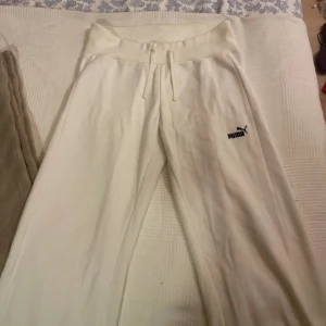 Vita mjukisbyxor från Puma - Snygga vita mjukisbyxor från Puma med bred ribbad midja och dragsko. Byxorna har en avslappnad passform, raka ben och en bakficka. Puma-logga broderad framtill.